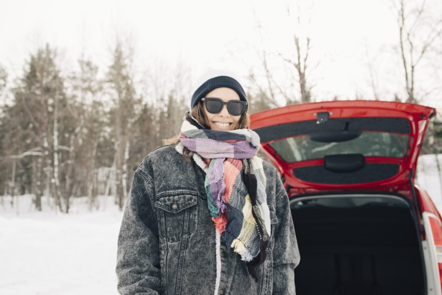 Kvinne med solbriller som står smilende foran bil